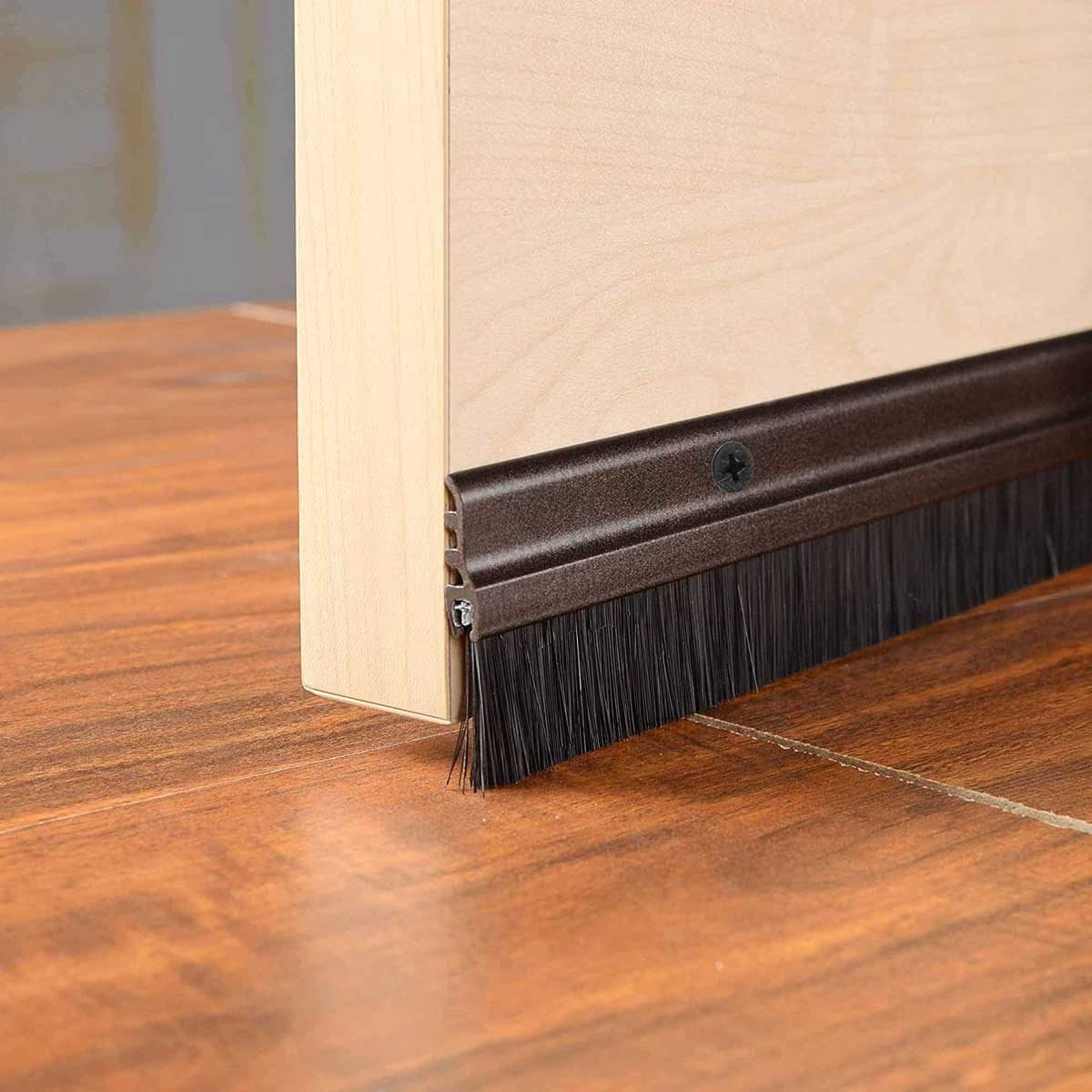 A door features a brown sweep attached to its bottom, brushing against wooden flooring, preventing dust or drafts from entering the room.