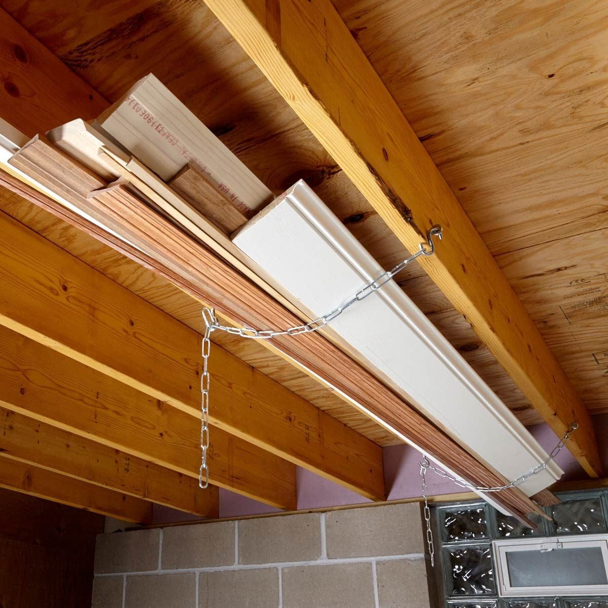 Wooden planks are suspended from a ceiling using chains, within a room featuring wooden beams and a concrete wall with a small window.