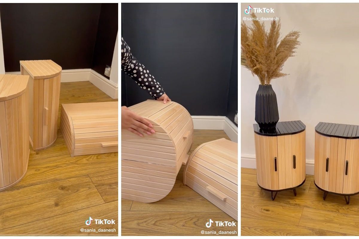 Wooden storage units are being arranged. They are set against a dark wall in a room with wooden flooring, showcasing modern furniture design