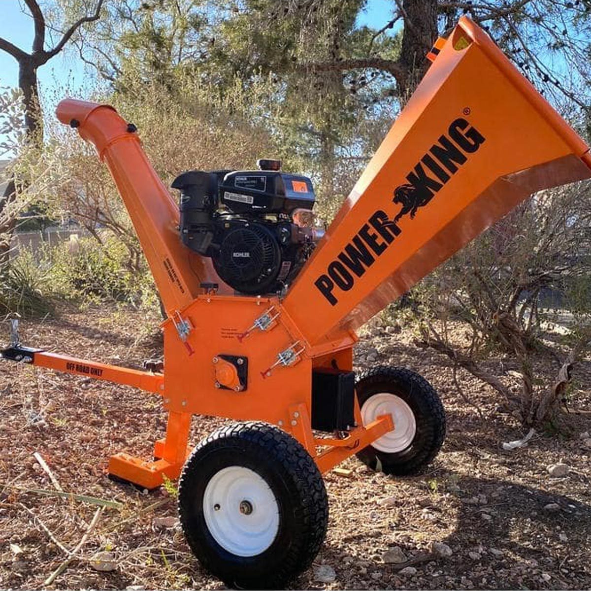 A bright orange wood chipper stands on wheeled legs, ready to shred branches and debris in a wooded outdoor area, surrounded by dry foliage