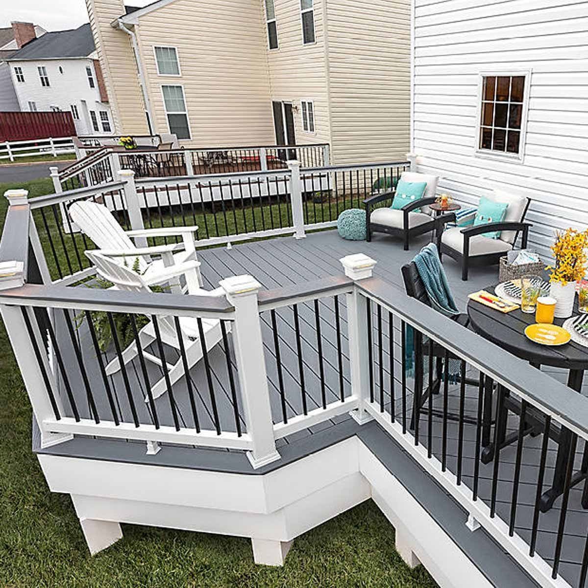 A deck features white and black furniture, a table with drinks and snacks, and a seating area, surrounded by grass and adjacent buildings.